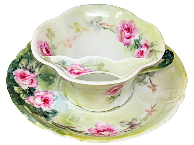 Scalloped cup and saucer with pink roses, green shading and a dark green handle; the moustache guard is visible inside.